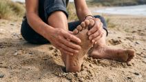 Devojka na plaži se drži za stopalo