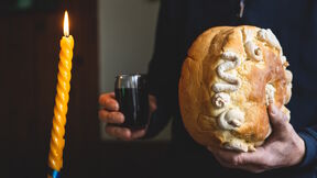 Čovek drži slavski kolač i vino pored upaljene sveće