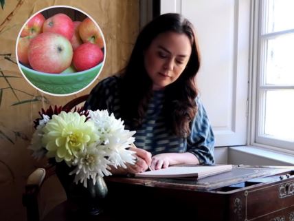zena pise jabuke i cvece na stolu
