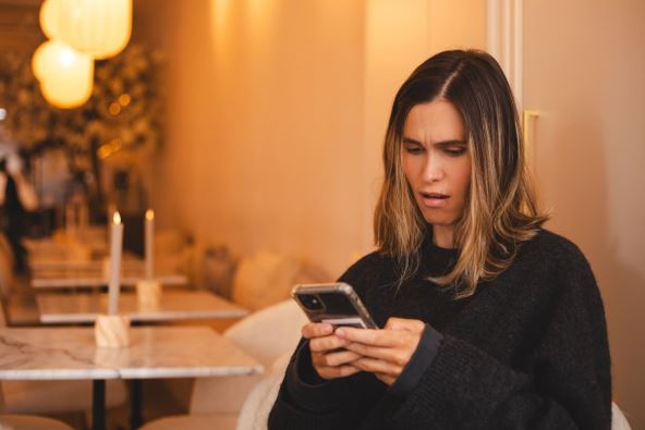 Iznenađena žena čita poruke na mobilnom