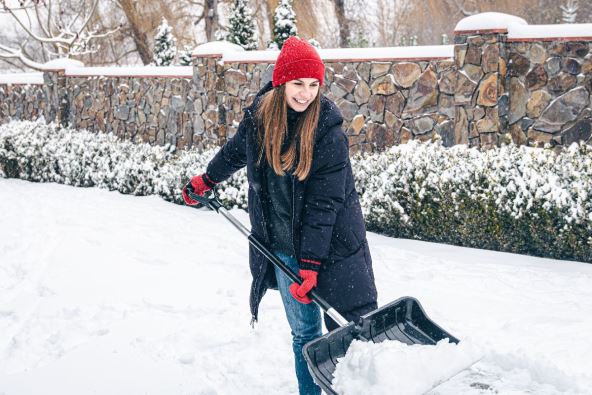 žena čisti sneg pred kućom